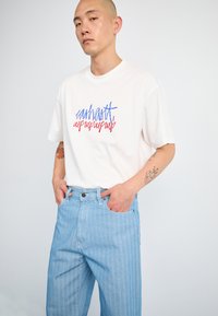 Hvit bomulls T-skjorte med fargerik, grafisk tekst. Kombinert med lyseblå stripete denimjeans med løs passform og sidelommer.