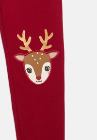 Rote Leggings mit einem braunen Rentiergesicht-Design, das Geweih, weiße Akzente und gestickte Details enthält, aus einer weichen Baumwollmischung gefertigt.