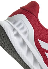 Red athletic shoe with a mesh upper, white midsole, and textured black rubber outsole, featuring slanted white accents on the side.