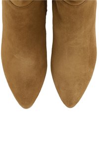 Bottines en daim marron avec un design à bout pointu et une texture lisse, présentant un style minimaliste et sans matériel visible.