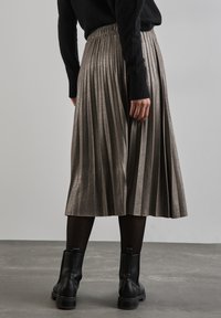 Metallic plisserad midiklänning med elastisk midja, tillsammans med svarta ankelstövlar, mot en neutral bakgrund.