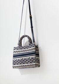 Kudottu olkalaukku, jossa on jämäkkä muoto, tummansinis-valkoinen raidallinen kuvio, koristeellinen yläkahva ja pitkä säädettävä olkahihna.