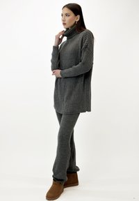 Suéter de punto acanalado gris con cuello alto, combinado con pantalones a juego de punto acanalado y botas de tobillo marrones. Presenta un corte relajado y una textura suave.