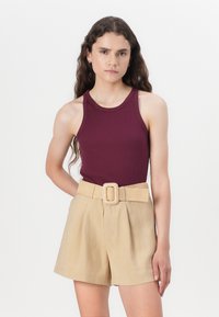 Maroon ribbed tank top with a round neckline paired with beige pleated shorts and a cream-colored textured belt with a square buckle.