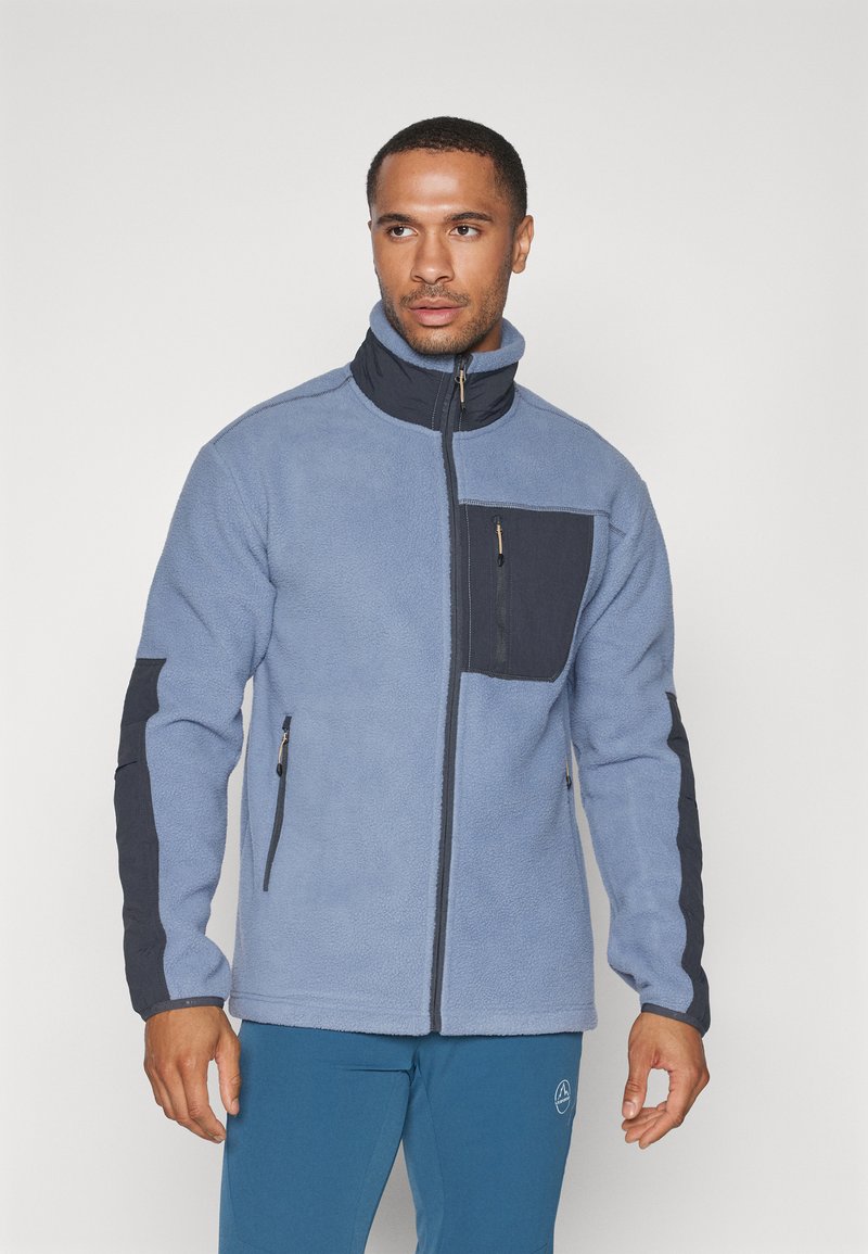 Kergest sinisest fleece-jakist kõrge kaelusega, tumehallide detailidega, tõmblukuga rinna taskuga ja küljetaskutega. Pehme tekstuur ja mugav lõige.