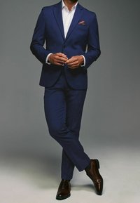 Granatowy garnitur o dopasowanym kroju, biały koszula i chusta w kieszeni. Brązowe skórzane buty o delikatnym połysku. Gładka tekstura i nowoczesny design.