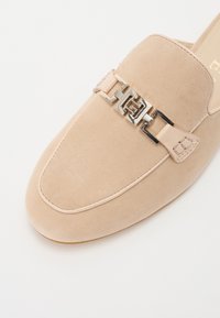 Pantofle din suede bej, cu accent din lanț metalic aproape de vârf, cu vârful neted și rotund și talpă cusută.
