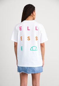 White cotton t-shirt with the word "WELLNESS" in pink, orange, and green letters; features a green half-circle graphic on the back.