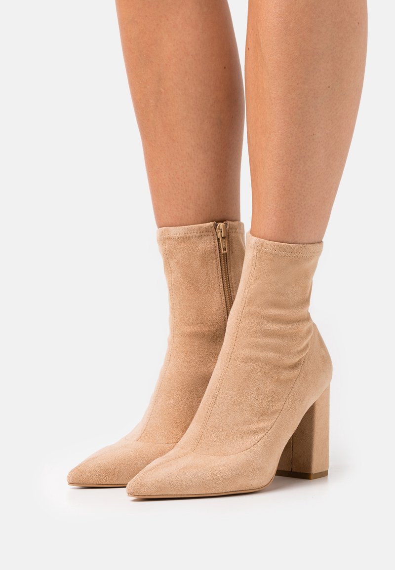 Bottines en daim nude avec bout pointu, haut talon bloc et fermeture éclair, présentant une texture froncée sur le dessus.