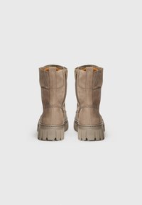 Bottines en daim marron avec une finition texturée, présentant une fermeture éclair sur le côté, un col rembourré et une semelle en caoutchouc épaisse.