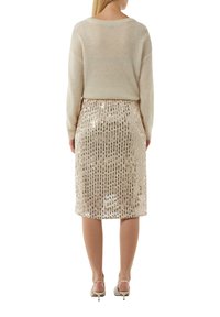 Beige gestrickter Pullover mit langen Ärmeln, kombiniert mit einem taillierten, paillettenbesetzten Bleistiftrock in hellem Beige. Silberne Akzente an den Absätzen.