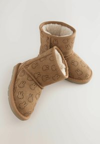 Bruna kängor med en mjuk inredning, med ett upprepat kaninmönster på utsidan. Rundad form med en texturerad sula för grepp.