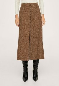 Falda midi marrón con lunares blancos, botones en la parte frontal y una abertura; combinada con botas negras de caña alta y punta. Textura de tela suave.