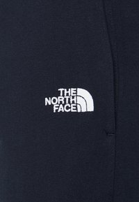 Námořnicky modrá látka s vyšívaným bílým logem The North Face v obloukovém provedení. Hladká textura, přiléhavý střih.