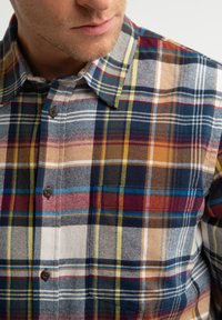 Plaid flanelinė marškiniai, kuriuose derinamos įvairios spalvos, įskaitant tamsiai mėlyną,raudoną, auksinę ir baltą. Jame yra mygtukiniai apykaklė ir matomi mygtukai.