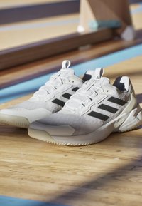 Białe buty sportowe z czarnymi akcentami, siateczkowa cholewka i teksturowana podeszwa. Posiadają wygodny design i zaczep na pięcie.