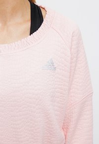Felpa rosa chiaro con motivo testurizzato, caratterizzata da un colletto arricciato e un logo adidas argento sul petto.