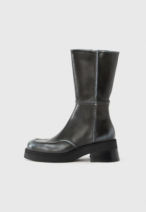 Črni usnjeni gležnarji z gladko teksturo, okrogel prst in blok peto. Z značilnim kontrastnim šivom in elegantnim, minimalističnim dizajnom.