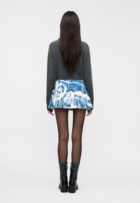 Γκρι πουλόβερ, πλισέ φούστα με μπλε και λευκό μοτίβο, μαύρο αδιαφανές καλσόν και μαύρες μπότες μέχρι το γόνατο. Λείο υλικό με στρωμένο σχέδιο.