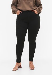 Pantalones negros ajustados hechos de una tela elástica, con una cintura alta, bolsillos laterales y una textura suave. Combinados con una blusa marrón.