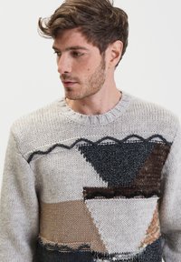 Maglione lavorato a maglia con collo rotondo, motivo geometrico in grigio, marrone e nero, con sezioni testurizzate e una finitura morbida e spessa.