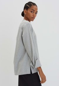 Haut gris à manches longues en tissu doux et texturé. Présente des fentes latérales et des manches retroussées, conçu avec une coupe décontractée.