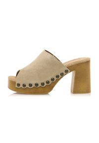 Mules de ante beige con puntera abierta y borde festoneado, adornados con tachuelas negras redondas y que presentan un tacón de madera grueso.