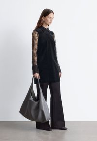 Schwarze Tunika mit durchsichtigen Spitzenärmeln, kombiniert mit dunklen, weit geschnittenen Hosen. Eine große graue Hobo-Tasche rundet das Outfit ab. Sanfte Texturen und schlichte Linien.