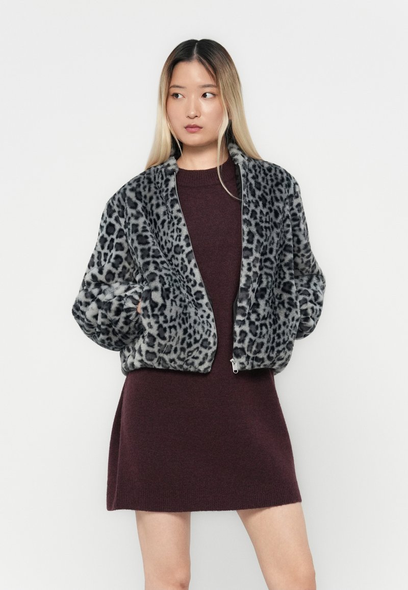 Bomberjacke aus Leopardenmuster-Faux-Fur mit langen Ärmeln und einem Reißverschluss auf der Vorderseite, kombiniert mit einem figurbetonten burgunderroten Strickkleid. Weicher Stoff, lässiges Design.