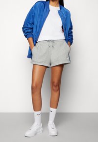 Chaqueta bomber azul sobre una camiseta blanca, combinada con pantalones cortos grises. Zapatillas y calcetines blancos, mostrando un look casual y deportivo.