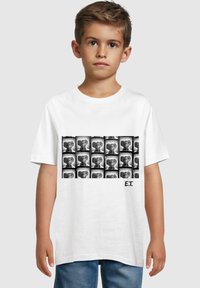 Hvid bomulds T-shirt med et sort-hvidt print af E.T.'s ansigt i et gittermønster, med "E.T." trykt i sort nederst til højre.