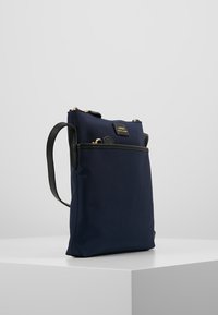 Borsa a spalla in tessuto blu navy con hardware dorato e un accento testurizzato nero. Presenta una tasca frontale e una tracolla regolabile per maggiore comodità.