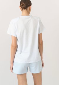 Biała bawełniana koszulka z krótkim rękawem i luźnym krojem, w połączeniu z jasno niebieskimi sportowymi szortami o gładkiej fakturze i prostym kroju.