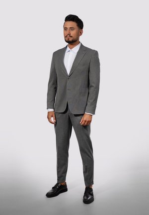 Gray tailored suit with a notch lapel, single button, and two front pockets. White dress shirt underneath, paired with black shoes.