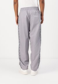 Grijze sportbroek met een elastische tailleband, zijstreep met een geometrisch patroon en een achterzak met de tekst "Milano 1978".