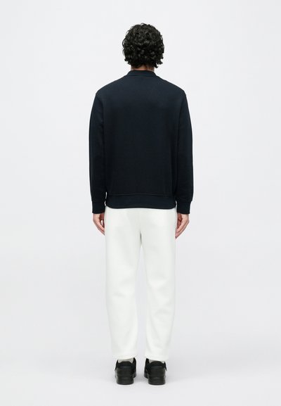 Granatowa bluza dresowa z okrągłym dekoltem, ściągaczami na rękawach i u dołu, połączona z białymi, zwężanymi spodniami dresowymi oraz czarnymi sneakersami. Prosty, minimalistyczny design.