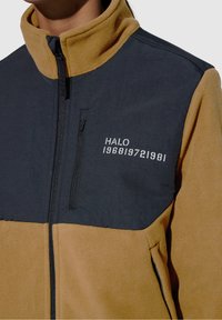 Fleece jacket in navy and mustard with a high collar, zippered pocket, and "HALO 196819721981" text detail on the chest.