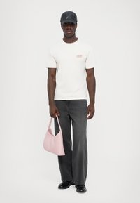 Light pink shoulder bag with a smooth texture, worn by a person in a white t-shirt and dark denim jeans, set against a plain background.