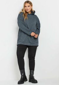 Sudadera gris carbón de corte relajado, con bolsillo frontal y cordones. Combinada con pantalones ajustados negros y botas de tobillo negras.