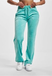 Turkusowe dresowe spodnie z weluru z elastycznym paskiem w talii, dwoma przednimi kieszeniami i prostym krojem nogawek. W połączeniu z białymi trampkami.