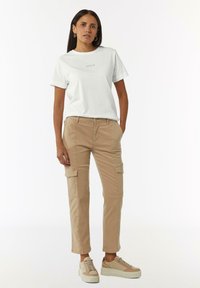 White cotton t-shirt with "Voila" text, paired with beige cargo pants featuring pockets. Beige sneakers complete the outfit.