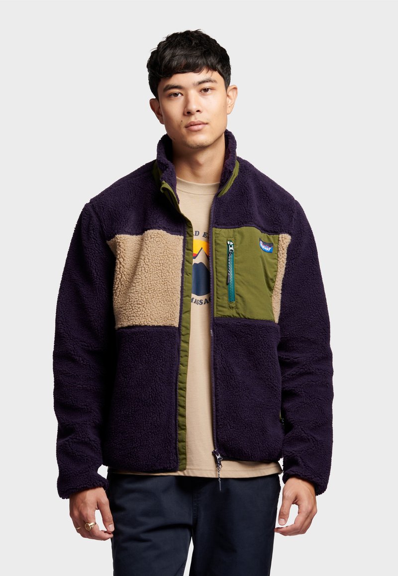 Fleece jacket featuring a purple body, tan and green panels, zippered chest pocket, and elastic cuffs, providing a textured design.