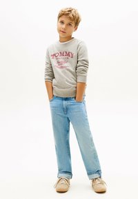 Szary sutener z logo "TOMMY HILFIGER", niebieskie dżinsy i beżowe sneakersy. Luźny krój z prążkowanymi mankietami i pasem.