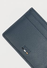 Sininen nahkainen korttikotelo, jossa on teksturoitu pinta, kaksi korttipaikkaa ja kohokuvioitu "BOSS"-logo, jonka alla kolme värikorostetta.