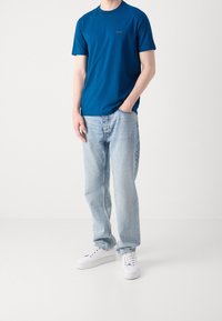 Modrá bavlněná tričko s krátkými rukávy, kulatým výstřihem a decentním logem. Spárováno s světle modrými rovnými džíny a bílými teniskami.