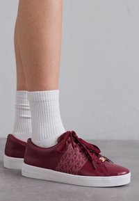 Burgundy nahkakengät valkoisilla kumipohjilla, kyljessä monogrammikuosi ja yhdistehengitysohjeet, käytettynä valkoisten ribbikuvioisten sukkien kanssa.