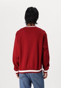 Sudadera roja con textura acanalada, rayas blancas en el escote y los puños, y un corte relajado. Combinada con jeans de mezclilla.