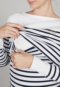 Gestreepte lange mouwen top in wit en marineblauw, met een rekbare stof, een ronde halslijn en een gouden logo accent op de borst.