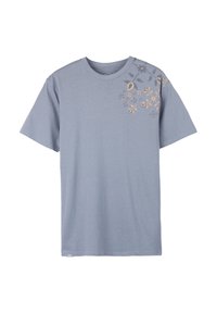 T-shirt bleu clair à manches courtes avec col rond et petit motif floral doré et gris sur l'épaule gauche.