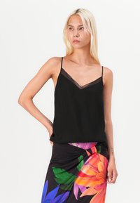 Camisola nera con spalline sottili e scollatura a V trasparente, abbinata a una gonna colorata con motivo floreale caratterizzata da un mix di colori vivaci.